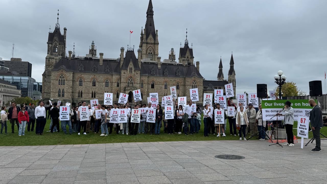 Community rally at Parliament Hill, Ottawa — applicants holding signs showing months waiting for IRCC response