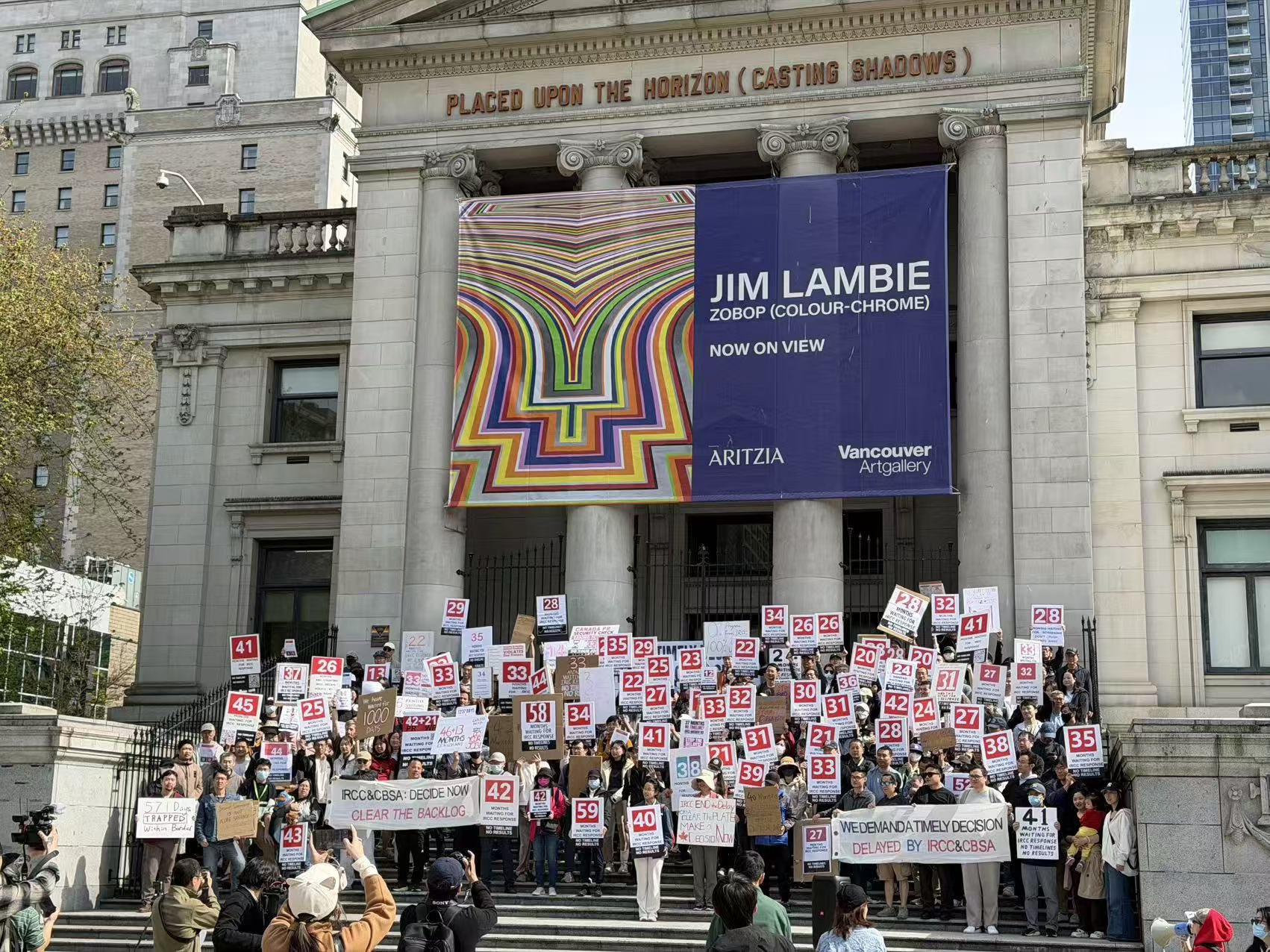 Community rally at Vancouver Art Gallery — applicants holding signs showing their wait times in months